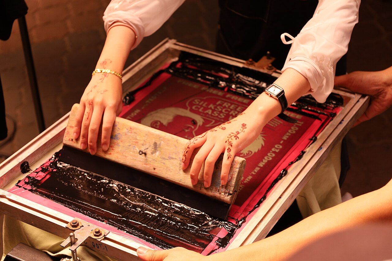 Hands pulling ink across a screen printing frame